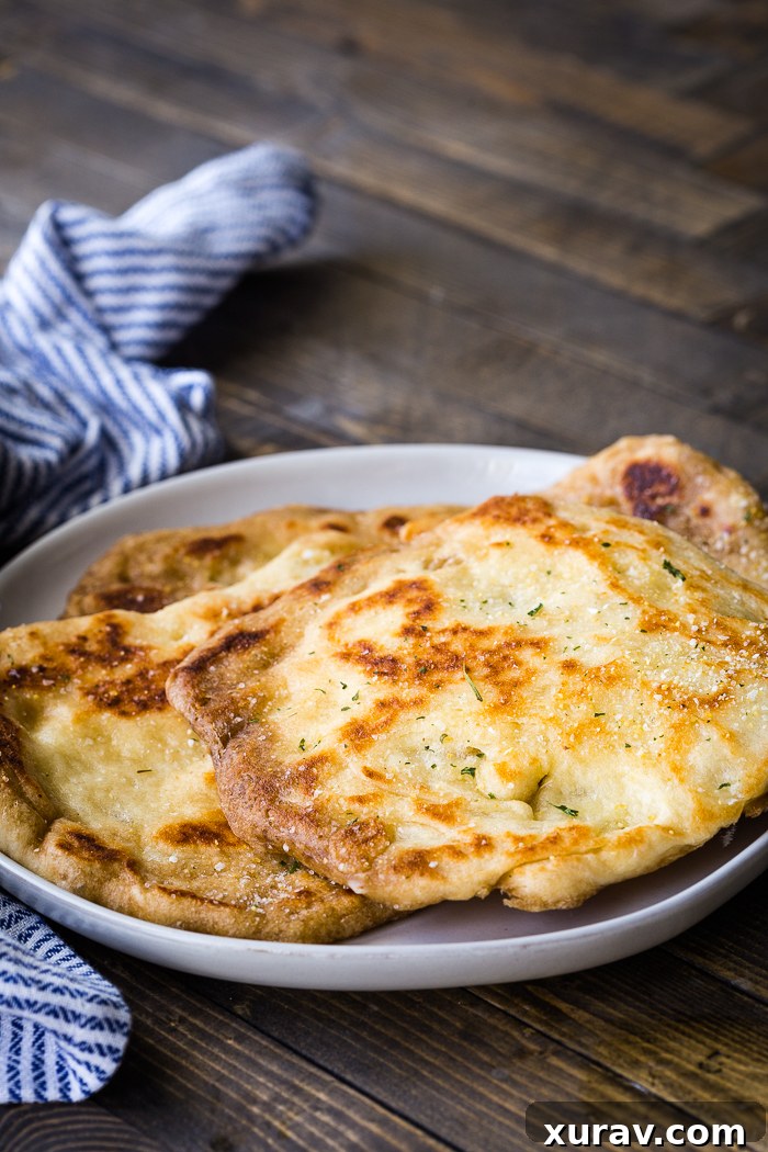 Golden-brown homemade naan bread resting on a white plate, showcasing its soft, pillowy texture, ready to be served.