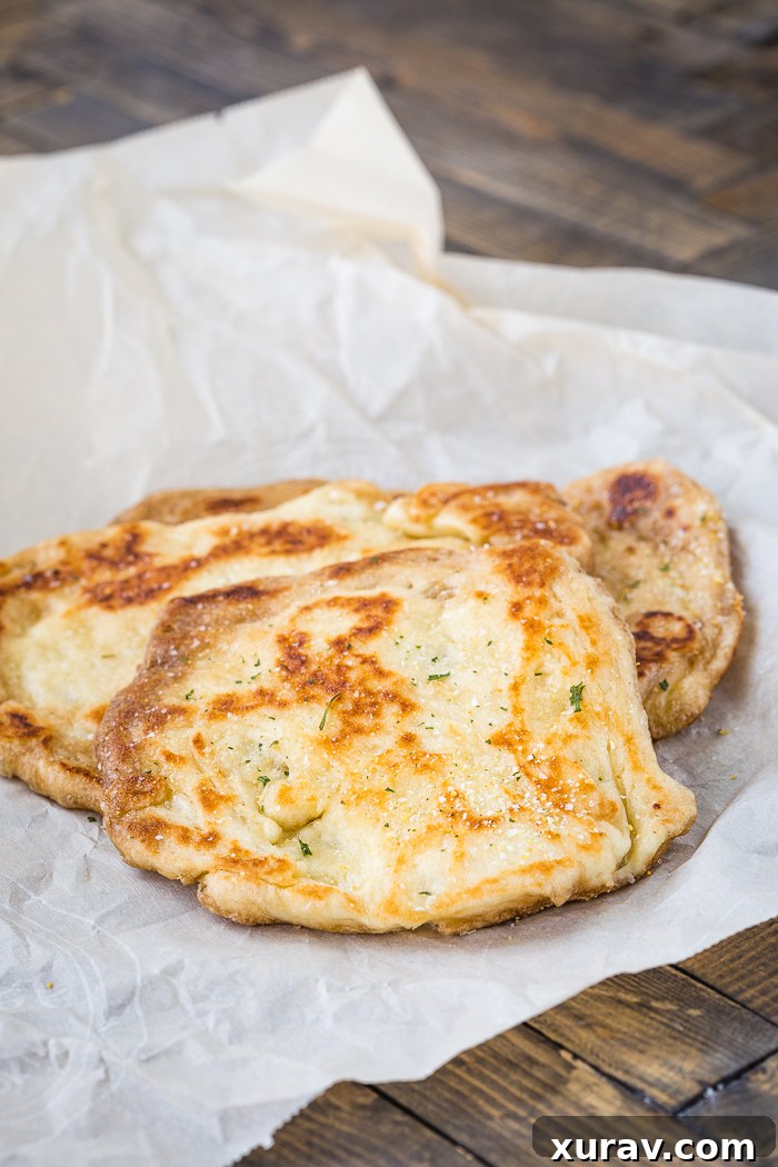 A stack of freshly cooked, warm naan bread pieces on wax paper, lightly brushed with butter and ready to be enjoyed as a side dish.