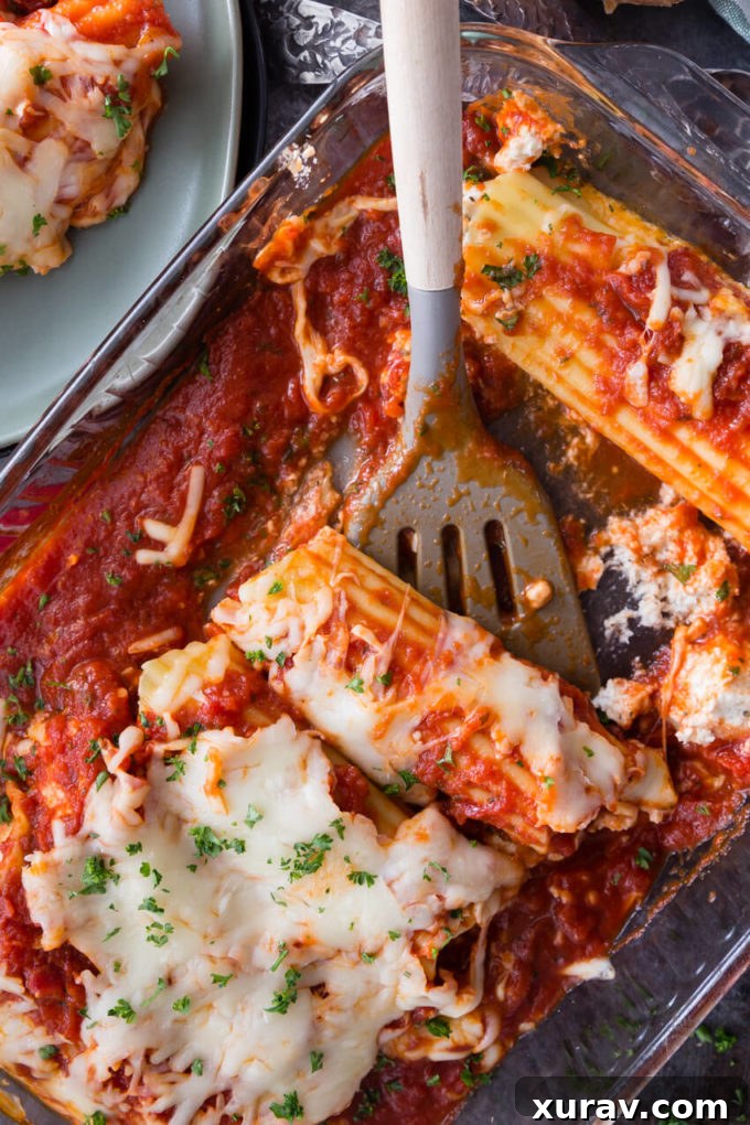 Cheese topped stuffed manicotti in a glass baking dish with a spatula