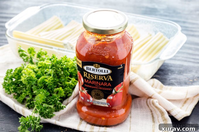 Bertolli pasta sauce in a jar on a dish towel with greens next to it and stuffed manicotti behind it
