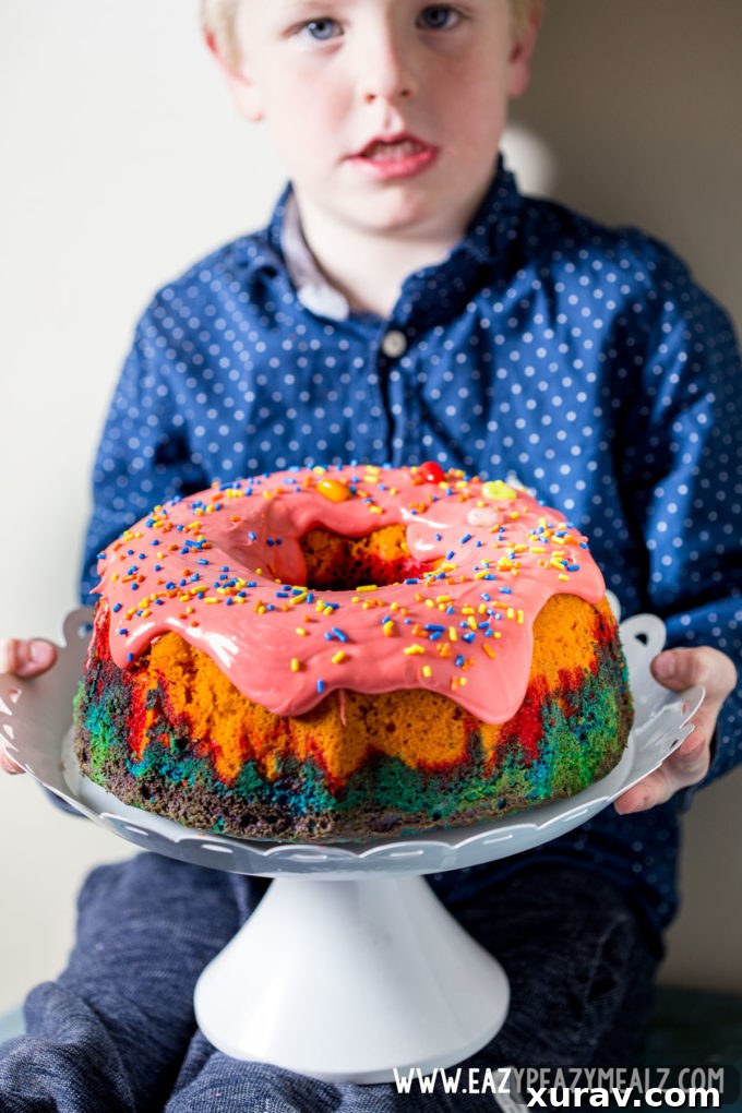 A young boy, Derrick, beaming with joy next to the vibrant Rainbow Bundt Cake, a testament to spontaneous celebrations.