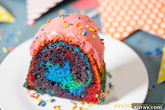 A close-up of a single slice of Rainbow Bundt Cake, revealing the distinct and colorful layers, topped with a glistening raspberry glaze.