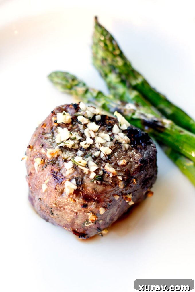 A serving of 10 Garlic Clove Marinated Grilled Filet Mignon sliced to reveal its perfect medium-rare doneness, served with grilled asparagus and corn.