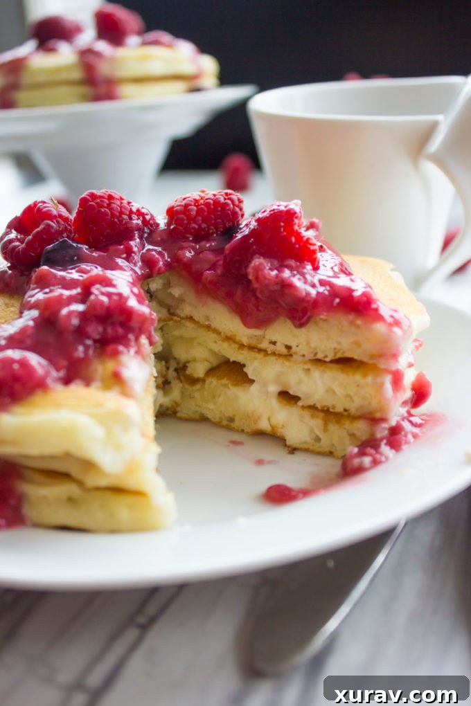 Freshly cooked Raspberry Cheesecake Pancakes stacked with berries and sauce