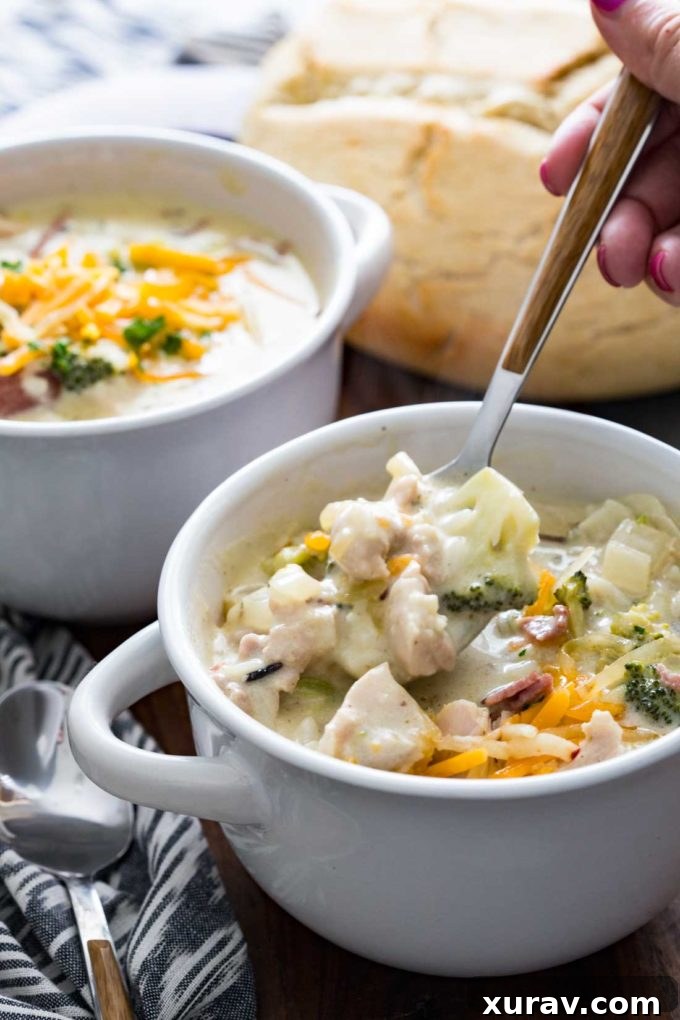 Close-up of a steaming bowl of Creamy Chicken, Bacon, Broccoli, and Cheddar Wild Rice Soup, topped with extra cheese and bacon bits.