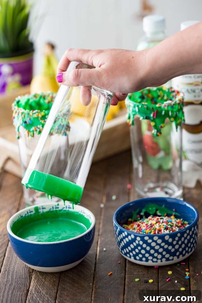 Close-up of a glass being dipped in green frosting and Halloween sprinkles for a festive punch presentation