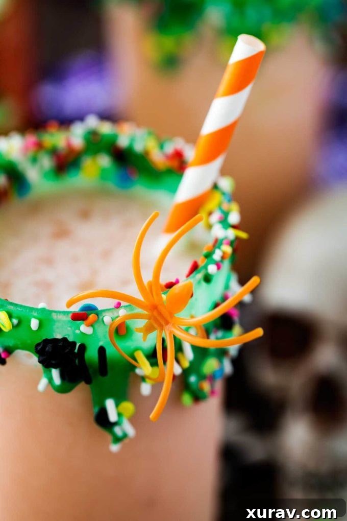 A festive glass of Swamp Potion Punch adorned with sprinkles and a plastic spider, ready for a Halloween party