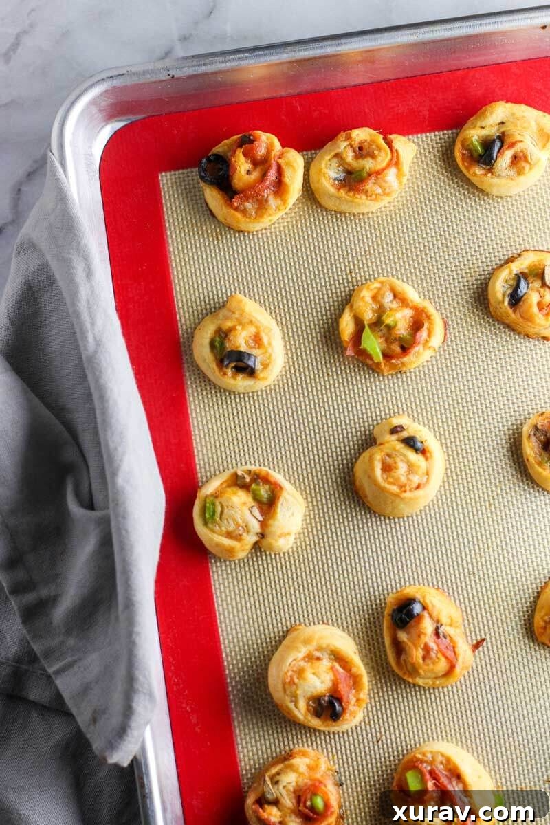 A tray of unbaked Supreme Pizza Pinwheels arranged on a baking sheet, ready for the oven.