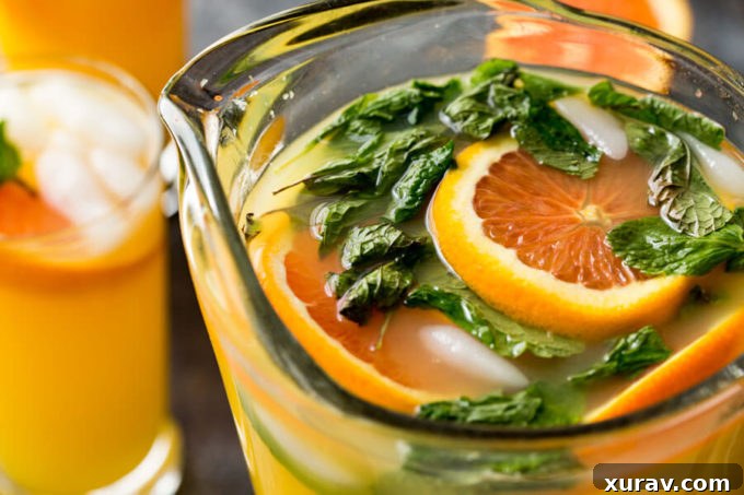 A pitcher of Mango Orange Mojito, filled with ice, orange slices, and mint leaves, ready to be poured into glasses.