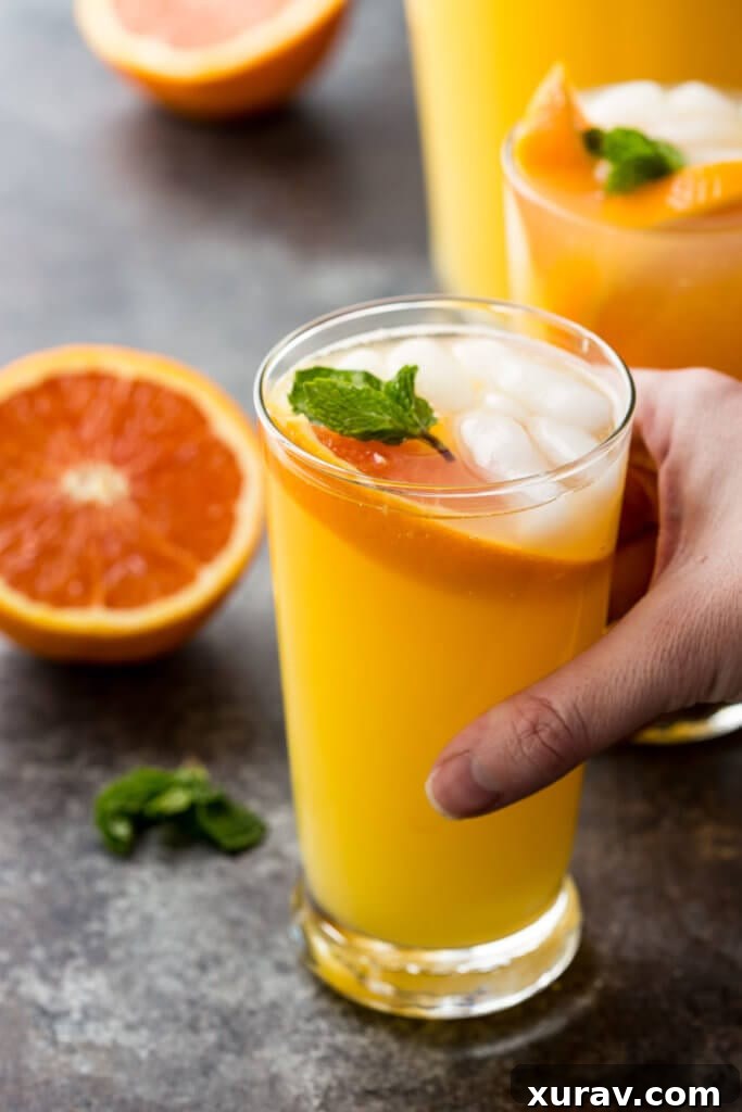 Four glasses of a vibrant Mango Orange Mojito, garnished with mint, orange, and lime slices, positioned on a rustic wooden table.