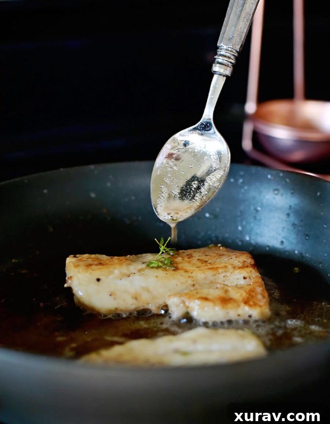 Close-up of pan-fried haddock fillet glistening with browned butter white wine sauce, showcasing its flaky texture.