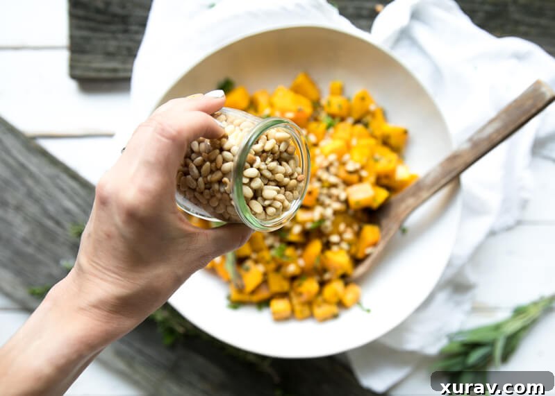 Butternut squash cubes being tossed in a bowl with olive oil, garlic, and herbs