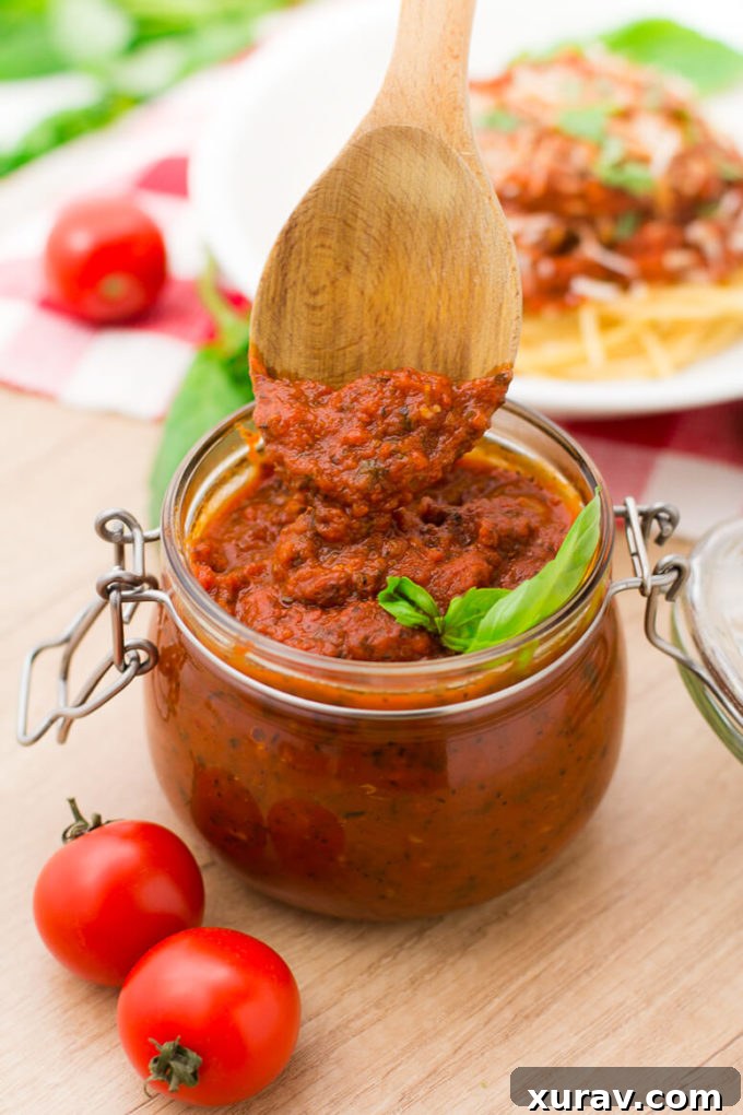 Homemade Spaghetti Sauce neatly stored in a glass jar, accompanied by a wooden spoon, perfect for future meals.