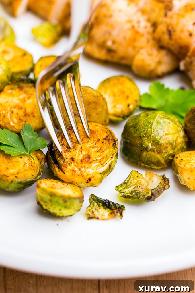 A mix of roasted chicken pieces and Brussels sprouts seasoned with herbs, arranged appetizingly on a clean white platter.