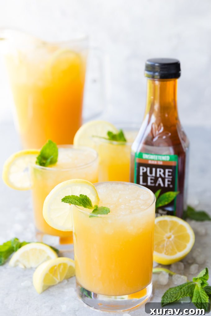 A few glasses of Mango Black Tea Lemonade with a lemon and mint garnish, and a pitcher of mango black tea lemonade in the background, as well as a bottle of Pure Leaf black tea on the side.