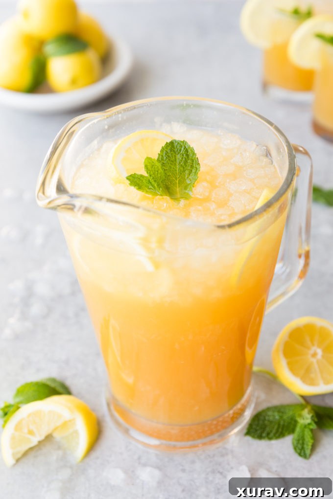 A glass pitcher of Mango Black Tea Lemonade with mint and lemon garnish
