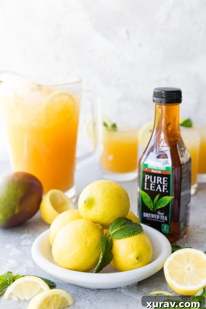 A white plate with lemons and mint, a bottle of pure leaf black tea, a mango, and a pitcher of Mango Black Tea Lemonade