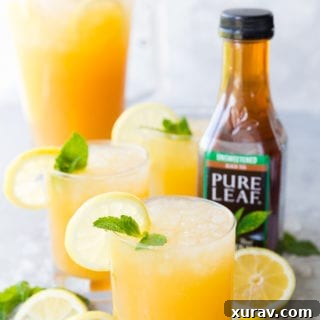 A few glasses of Mango Black Tea Lemonade with a lemon and mint garnish, and a pitcher of mango black tea lemonade in the background, as well as a bottle of Pure Leaf black tea on the side.