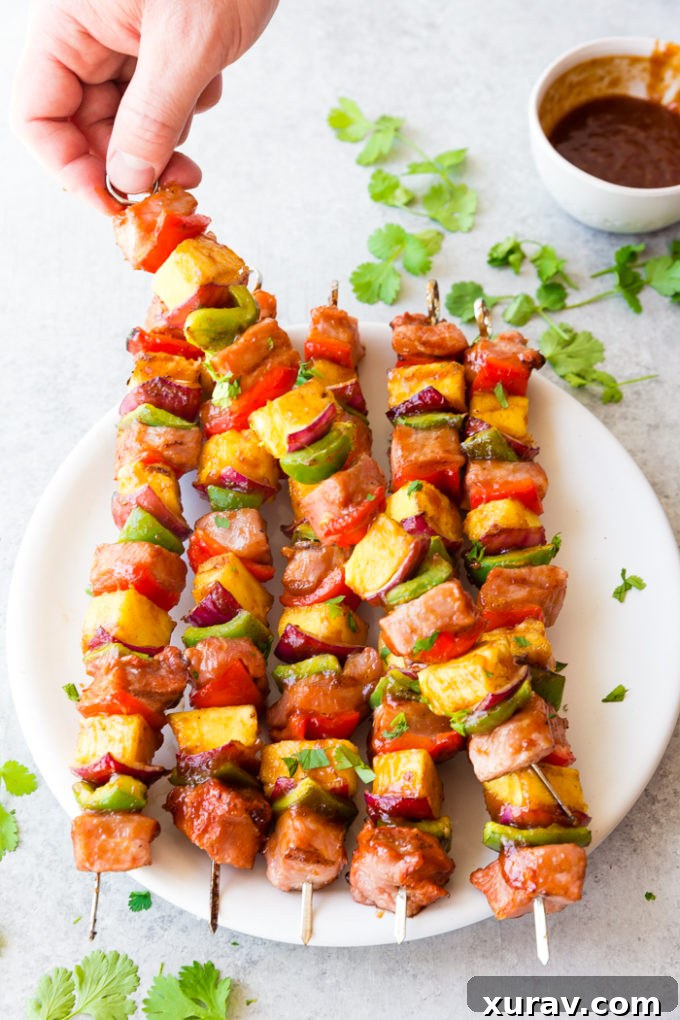 A white plate with 6 sticky bbq pork skewers cilantro, and bbq sauce for dipping