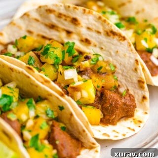 Three tacos al pastor with pineapple pico on top and lime garnish
