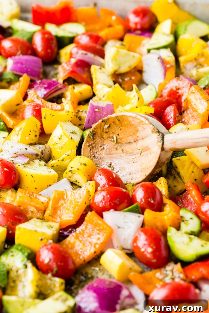 A sheet pan full of freshly chopped vegetables, coated in seasoning and olive oil, ready to be placed in the oven for roasting.