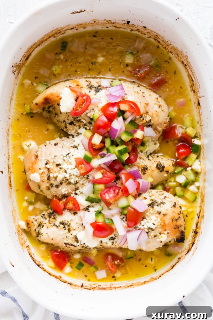 Baked Greek Chicken Breast garnished with fresh herbs and lemon slices.