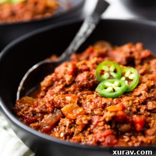 a black bowl full of keto chili, topped with jalapenos. This low carb chili has a spoon in it.