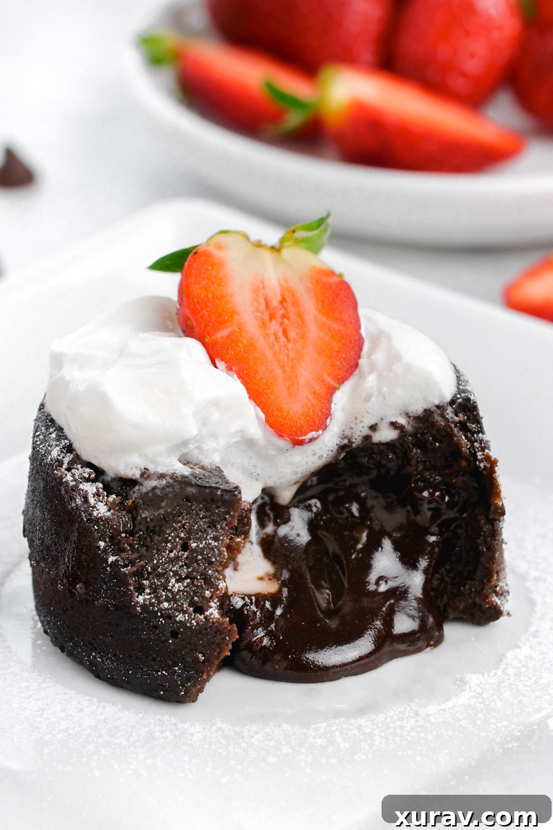 Decadent chocolate molten lava cake, with a stream of molten chocolate oozing out, beautifully topped with fresh whipped cream and vibrant strawberries.