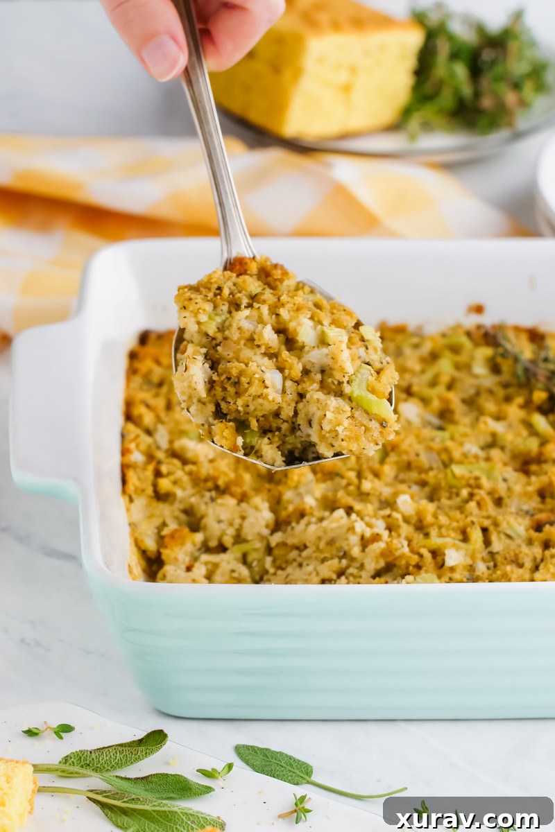 A generous portion of cornbread dressing in a white casserole dish, garnished with fresh rosemary, ready to serve.