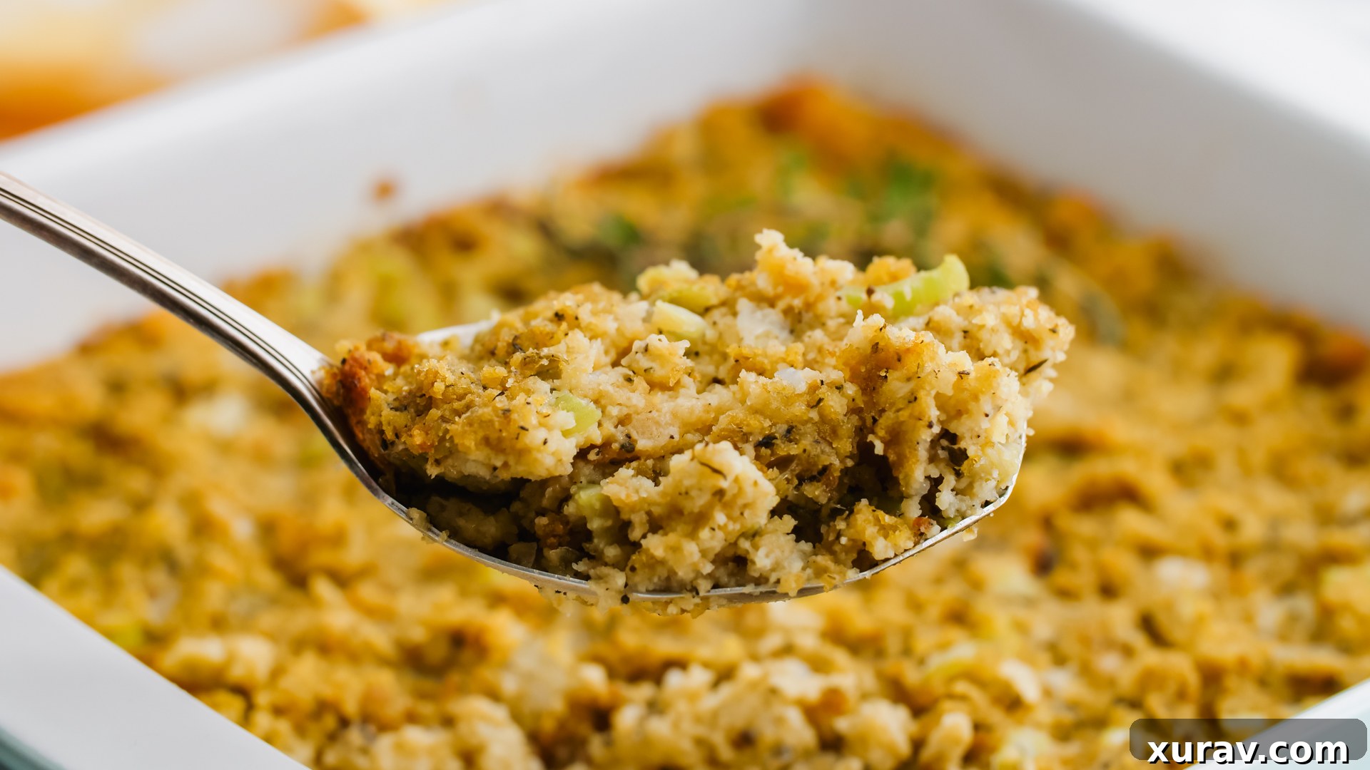 A spoon scooping a fluffy, golden portion of cornbread dressing from a dish, highlighting its comforting texture.