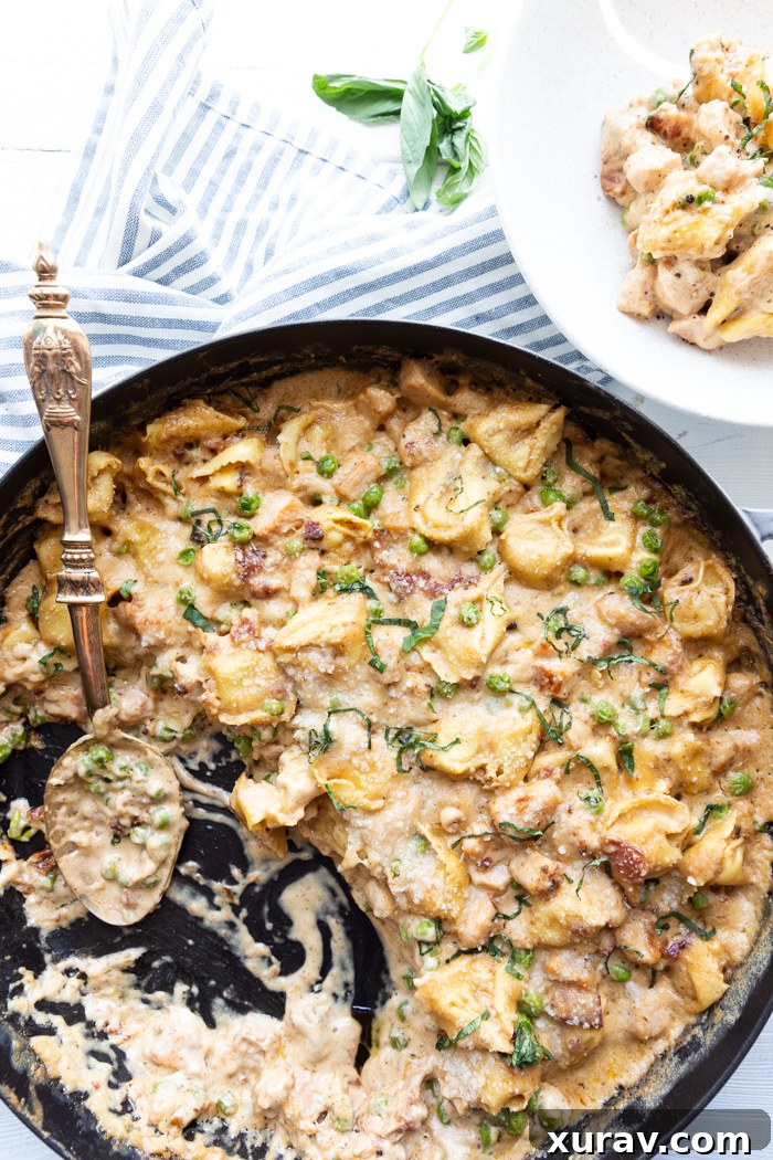 A large skillet filled with a creamy pork and tortellini bake, garnished with fresh herbs.
