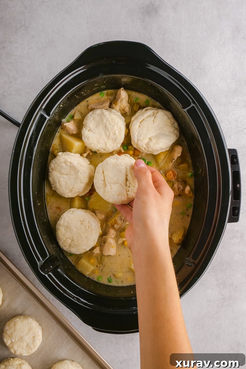 A bowl of slow cooker chicken pot pie with a biscuit, and ingredients on the side.