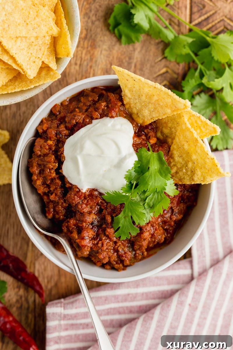 A large pot filled with rich, dark red chili con carne, garnished with fresh cilantro and a dollop of sour cream, ready to be served.