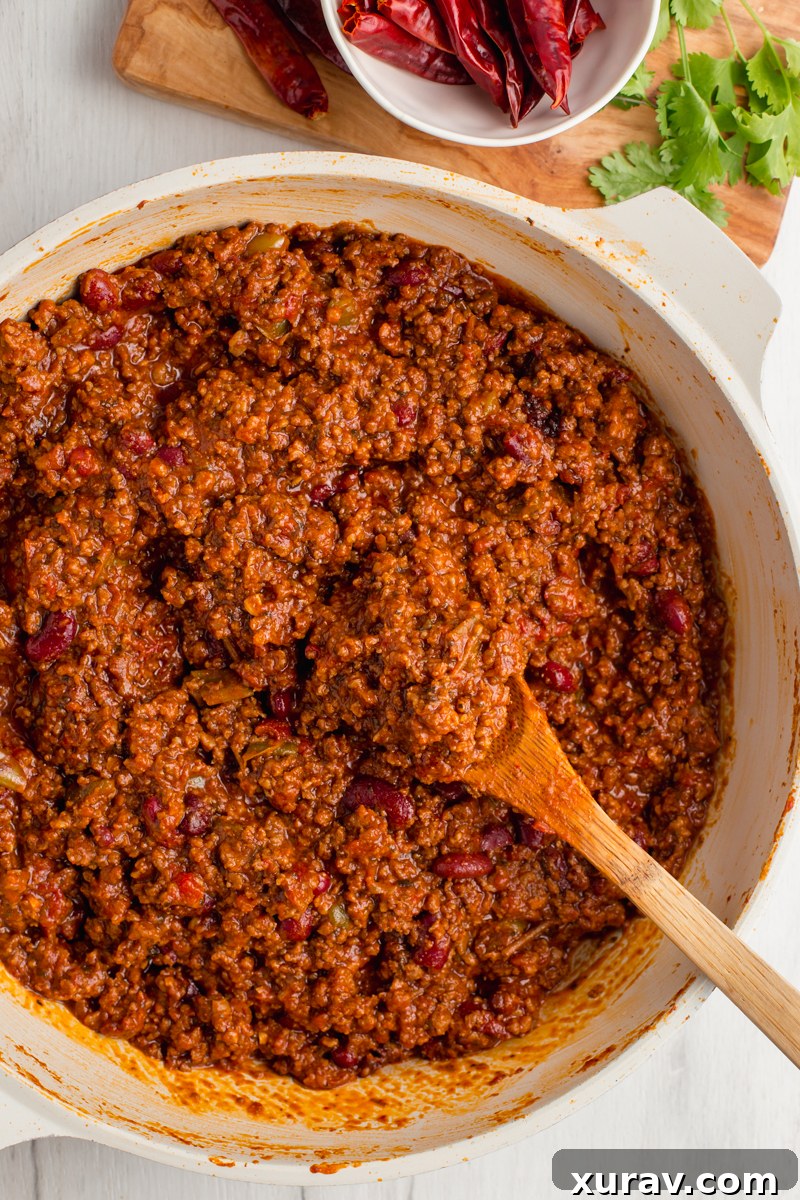 A close-up of the simmering chili con carne, showing the rich texture of the ground beef, diced tomatoes, and kidney beans, ready for the next steps.
