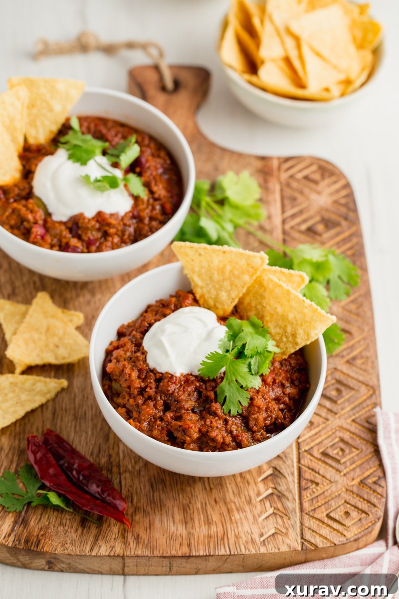 A bowl of thick chili con carne, garnished with shredded cheese and a dollop of sour cream, next to a spoon, inviting enjoyment.
