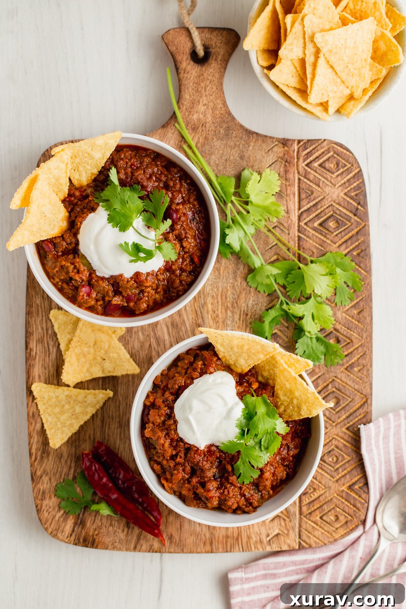 A vibrant bowl of chili con carne topped with generous amounts of shredded cheese, sour cream, and fresh cilantro, promising a delicious experience.