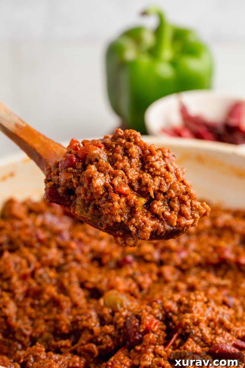 A warm, inviting bowl of chili con carne, garnished with cheese, green onions, and a side of golden cornbread.
