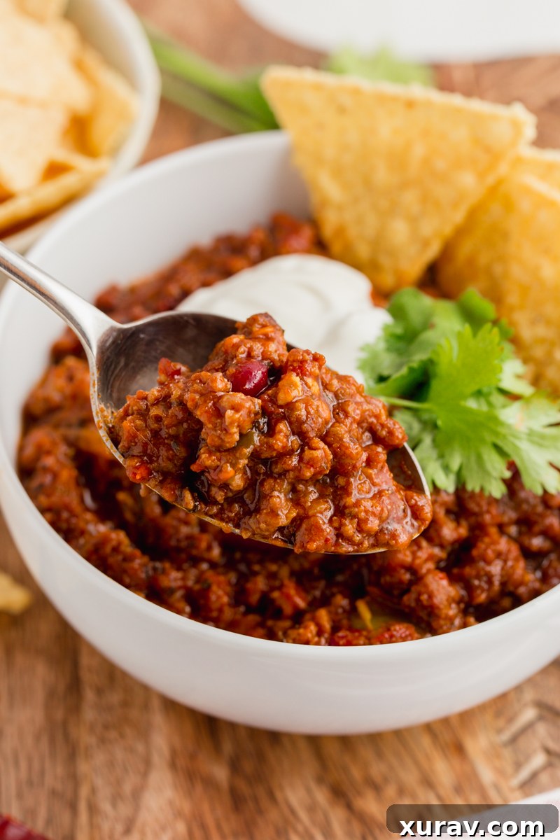 A close-up of a serving of chili con carne with a generous amount of shredded cheese and a dollop of sour cream, ready to be enjoyed.