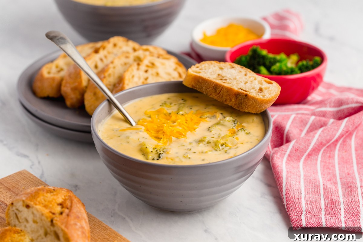 A top-down view of a bowl of creamy broccoli cheese soup, with a focus on the rich, inviting texture and color, served with a side of bread.