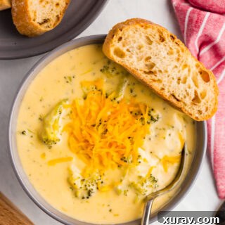 A close-up of a serving of creamy broccoli cheese soup, highlighting its rich texture and color, in a white bowl.