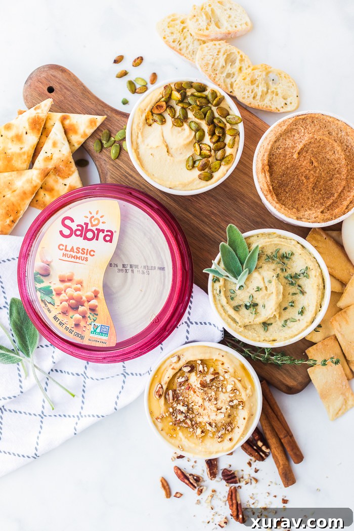 A vibrant display of four different flavored hummus dips arranged in a flight, with various dippers like apples, pita bread, and baguette slices.
