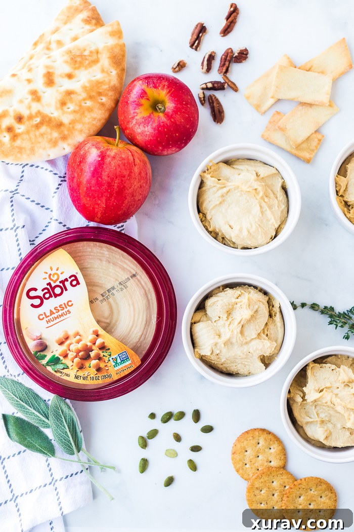 Close-up shot of a creamy pumpkin spice hummus topped with a sprinkle of pumpkin pie spice, served with fresh apple slices and pita bread.