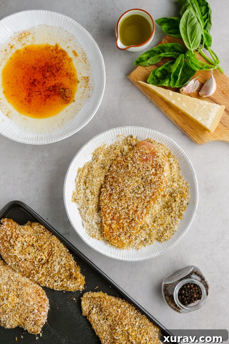 Close-up of baked breaded chicken breasts, golden brown and crispy, on a baking sheet with herbs.