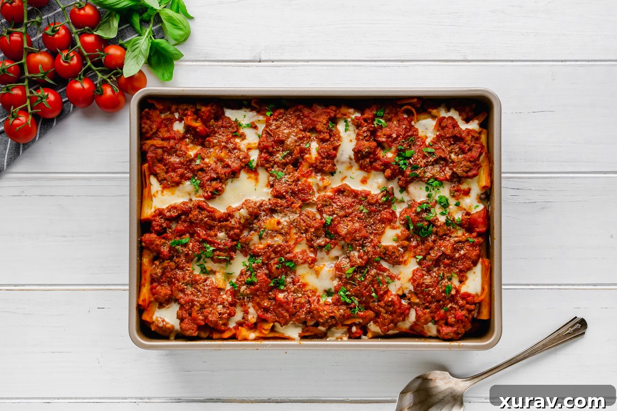 A close-up of a serving of baked ziti, showing the layers of pasta, meat sauce, and melted cheese, garnished with fresh basil.