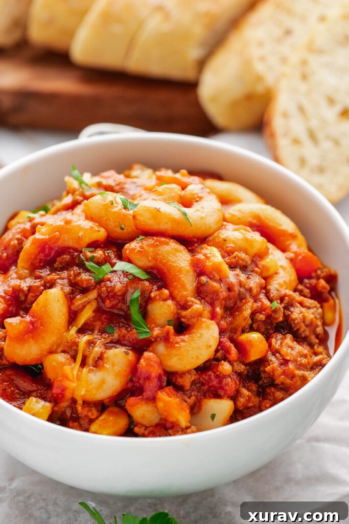 A steaming white bowl filled with classic Instant Pot American Goulash, featuring elbow macaroni, ground beef, and a rich tomato sauce.