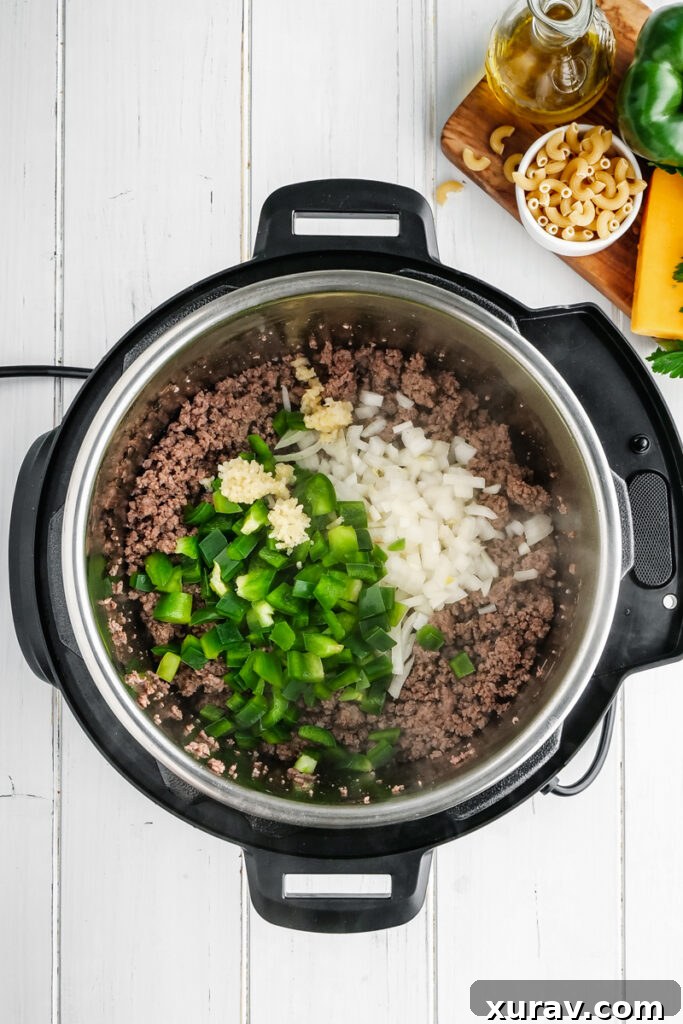 An Instant Pot filled with sautéed ground beef, diced onions, green bell peppers, and minced garlic, forming the flavorful base of American Goulash.