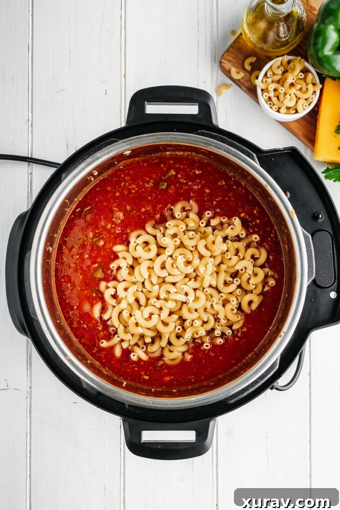 Uncooked elbow macaroni submerged in the rich tomato sauce and beef mixture within the Instant Pot, ready for pressure cooking.