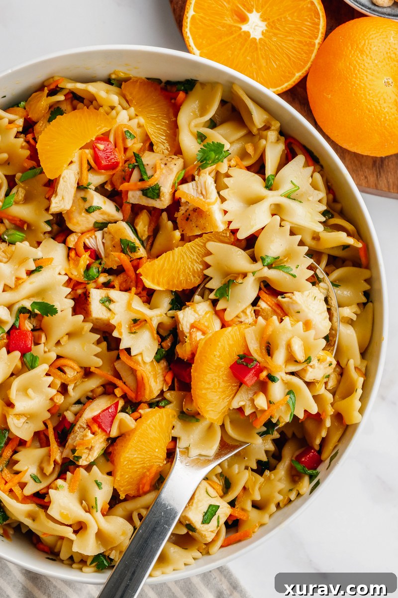 A white bowl with Asian pasta salad, oranges on the side.