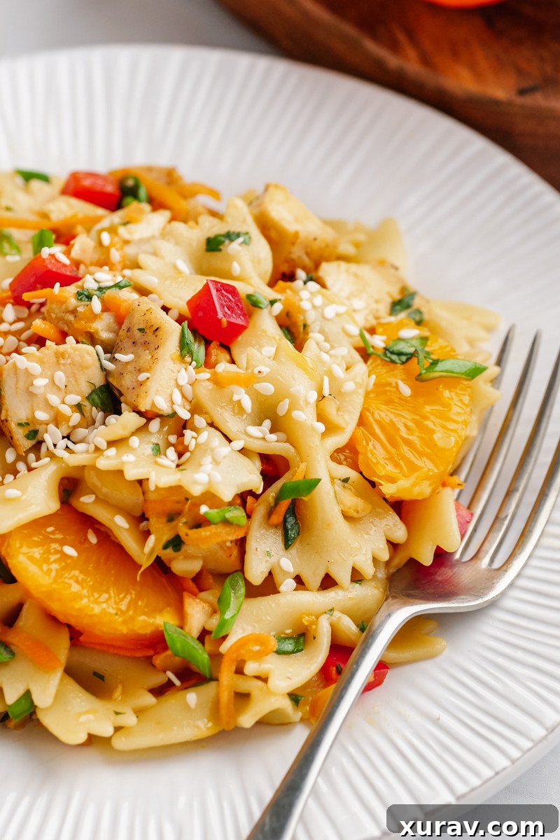 A white plate with a silver fork, pasta, mandarins, peppers, and green garnish.