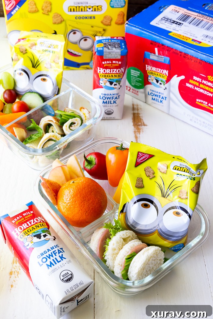 glass bento box with mandarin orange, grape tomatoes, carrot sticks and celery sticks, a round sandwich and a yellow package of Nabisco minion cookies, packaging for horizon organic low fat milk boxes and Nabisco Minion cookies behind